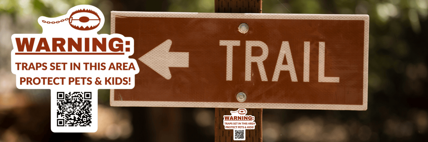 24.12.18 Trap Aware Banner A trail sign reads "Trail" with an arrow pointing left on a red background with white trim and text. A Wildlife for All sticker mocked up to be placed on the trail sign post. The sticker has an image of a trap at the top and a QR code at the bottom reads, "Warning: traps set in this area. Protect pets and kids."