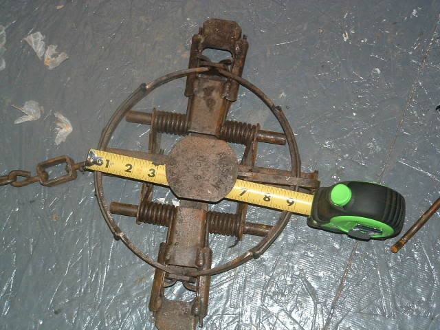 WOLF-TRAP-LEGHOLD-shared-by-Trap-Free-Montana-Public-Lands-Dec-16-2013 A leg hold trap is shown open on a concrete floor. A yellow tape measure spans the trap showing it is more than 9 inches wide.