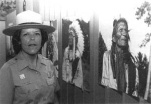 Barbara Sutteer (Booher) stands in front of a display at the Little Bighorn National Monument in her park ranger uniform, in a black and white image. She is a trailblazer for women in conservation as we celebrate women's history month.